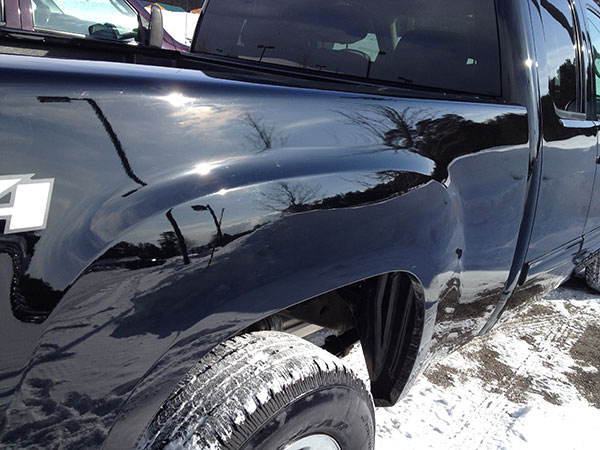 Dent repaired on the rear quarter panel above the wheel of a black pickup truck after paintless dent repair in Fife Lake, Michigan
