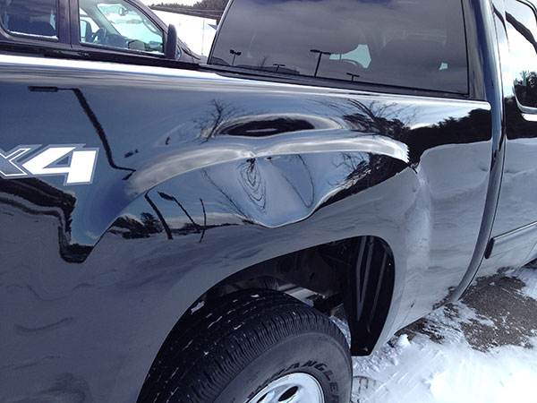 Dent visible on the rear quarter panel above the wheel of a black pickup truck before paintless dent repair in Fife Lake, Michigan