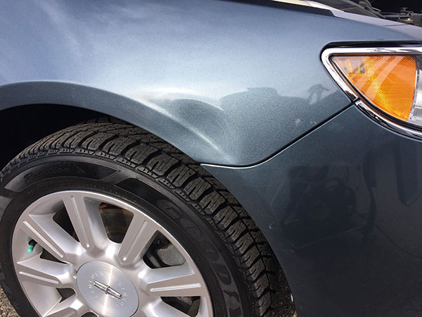 Dent visible on the front fender above the wheel of a blue sedan near the headlight.