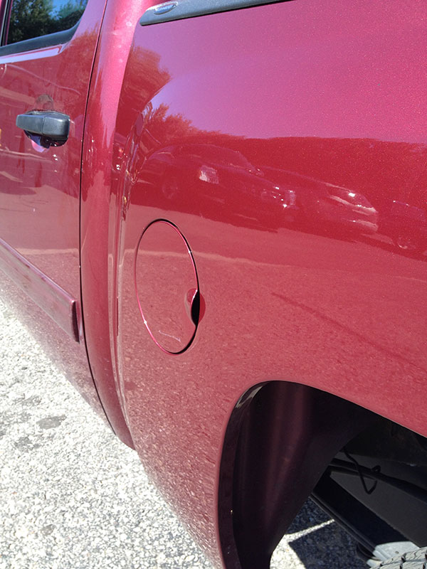 Red pickup truck bedside after paintless dent repair, showing a smooth panel where a shopping cart dent was removed.
