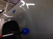 Large dent visible on a vehicle quarter panel with glue tabs attached, before paintless dent repair.