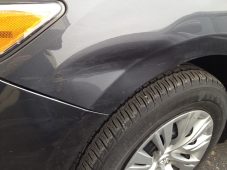 Front fender dent above the wheel before paintless dent repair on a dark gray sedan