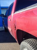 Dent visible on the bedside of a red pickup truck caused by a shopping cart before paintless dent repair.