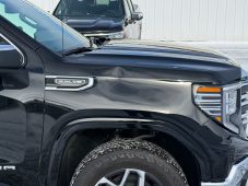 Black GMC Sierra pickup truck showing a dent on the front driver-side fender near the wheel well.